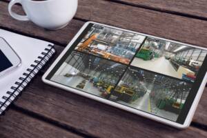 Tablet with views of warehouse from security cameras on screen lying on wooden table. security, safety, surveillance, and digital interface.