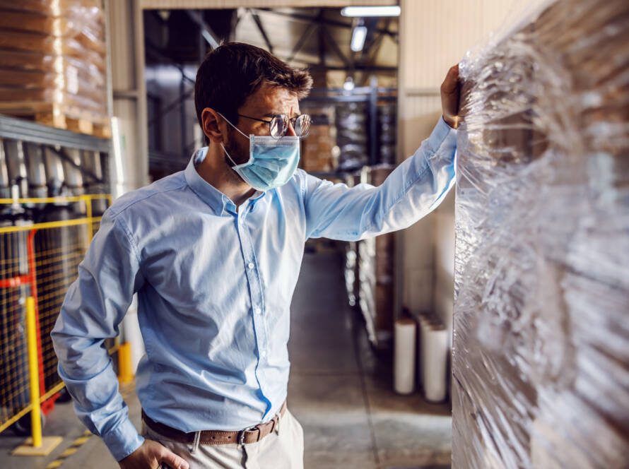 Young attractive businessman wearing protective sterile mask and checking out packed goods.
