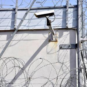 close up view of the corner of a prison with barb wire and a camera mounted on the side of the wall