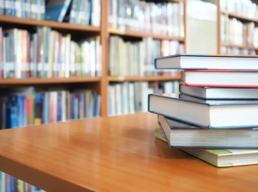 Book stack on wood desk and blurred bookshelf in the library room, education background, back to school concept