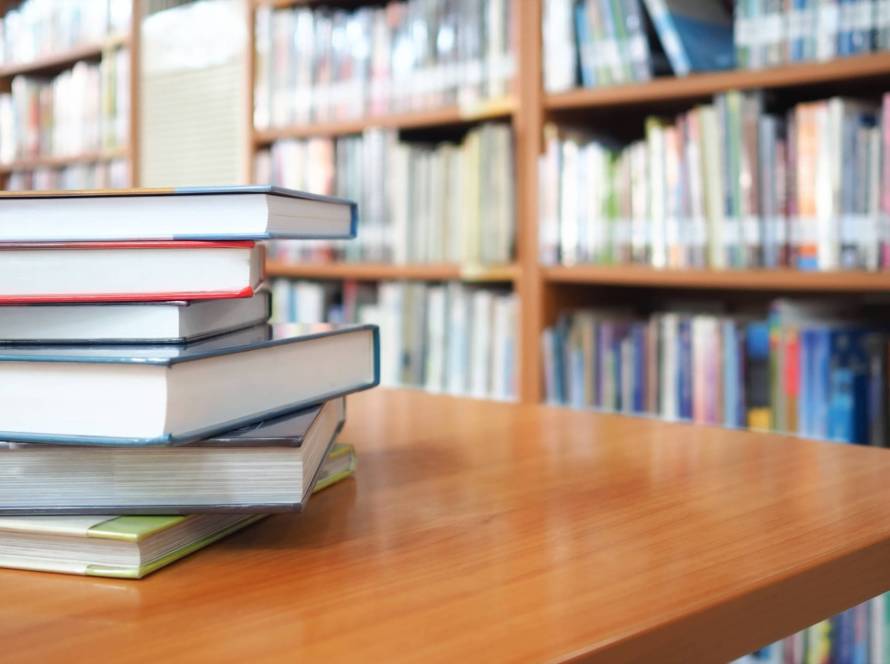 Book stack on wood desk and blurred bookshelf in the library room, education background, back to school concept