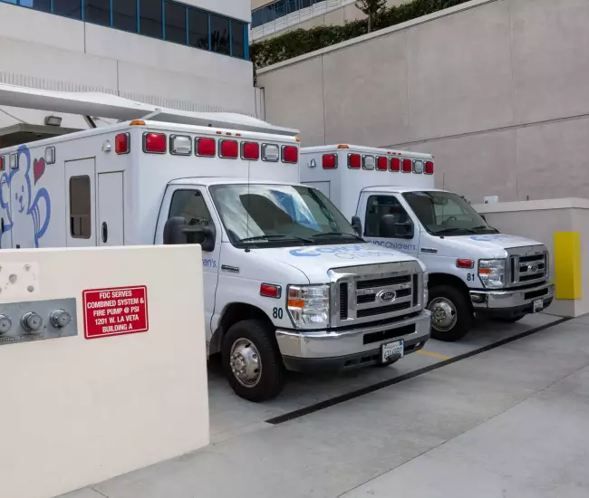 A pair of ambulance, or ambulances, parked in the back of a hospital docking bay, waiting area